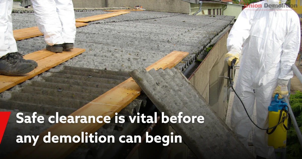 Workers in PPE clearing asbestos roofing before demolition.